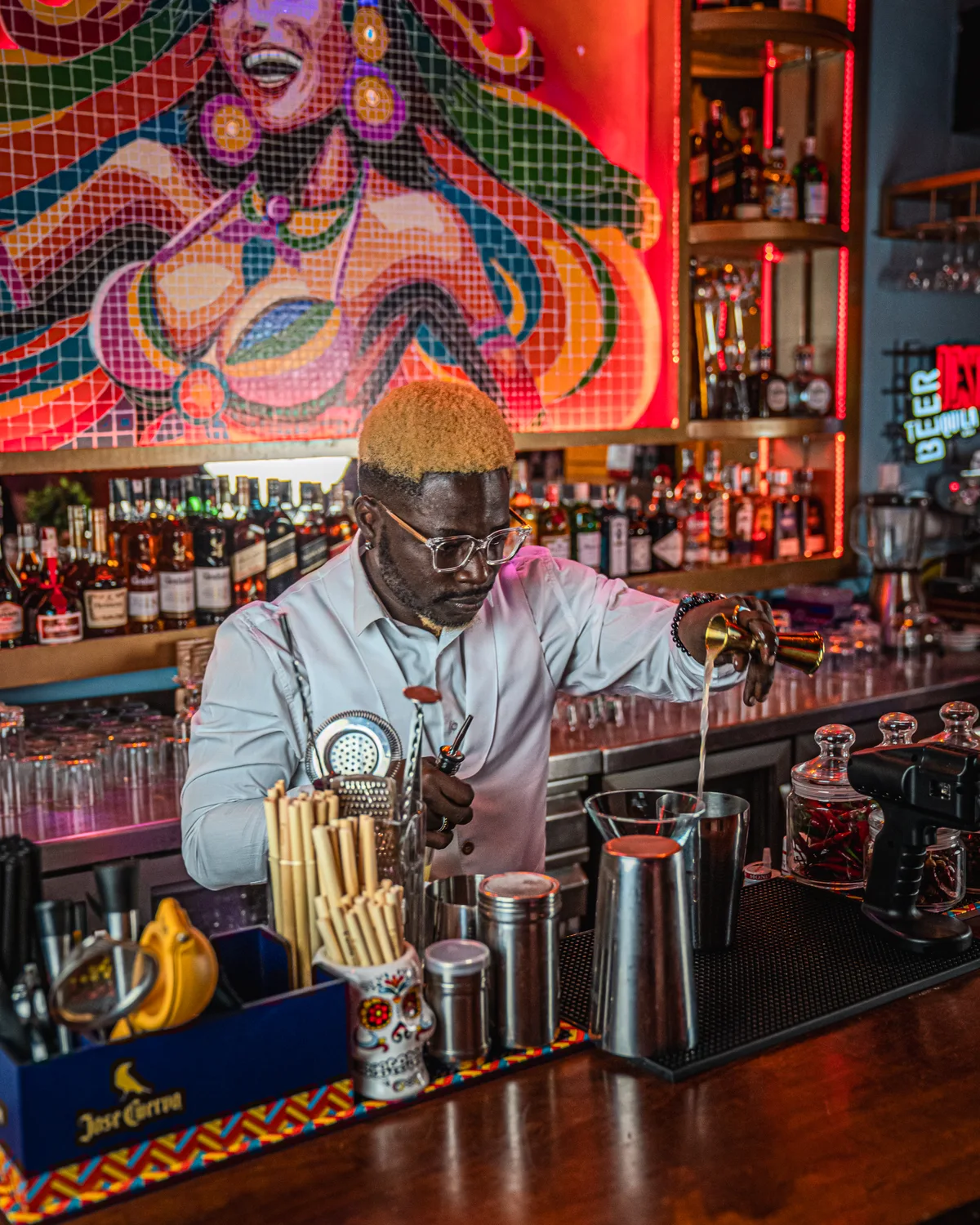 Bartender FavelaChic préparant un cocktail devant la fresque du bar, réalisé par HighFive
