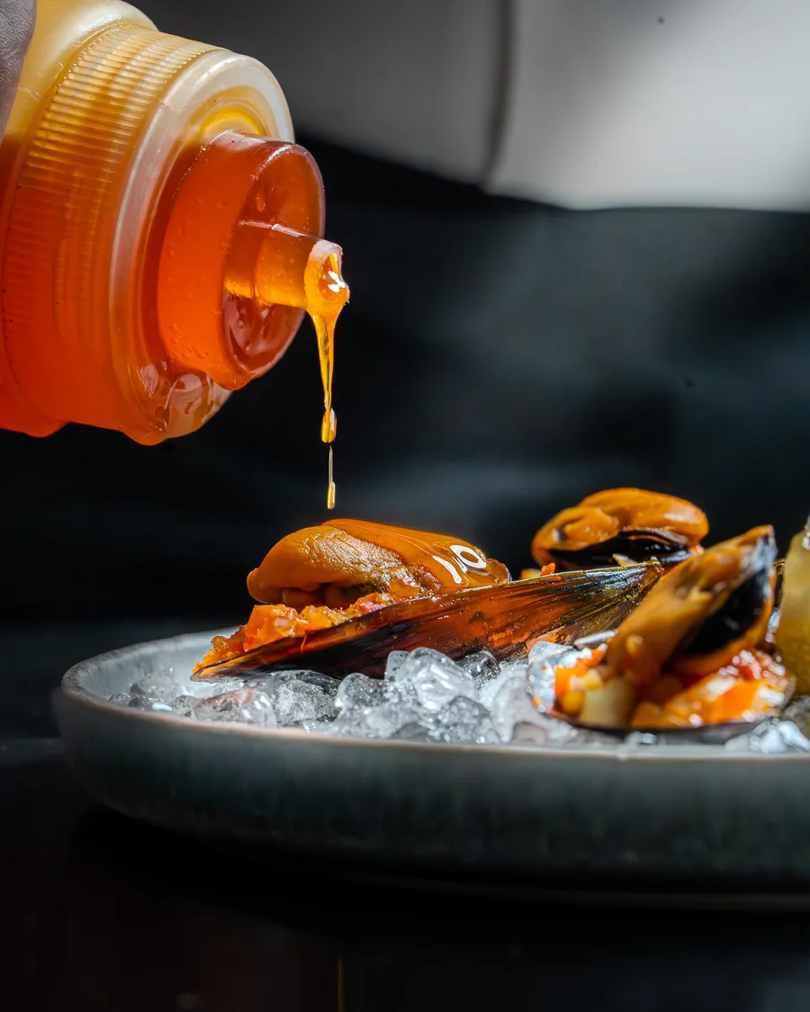Condiment ambré déposé sur une assiette de moules
